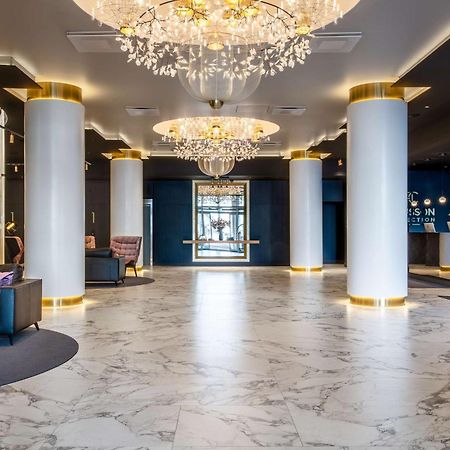 فندق راديسون بلو سكاي تالين المظهر الخارجي الصورة The photo shows a stylish hotel lobby with a modern design. It features elegant chandeliers hanging from the ceiling, which provide soft lighting. The floor is made of light-colored marble, adding a touch of luxury. In the foreground, there are dark 