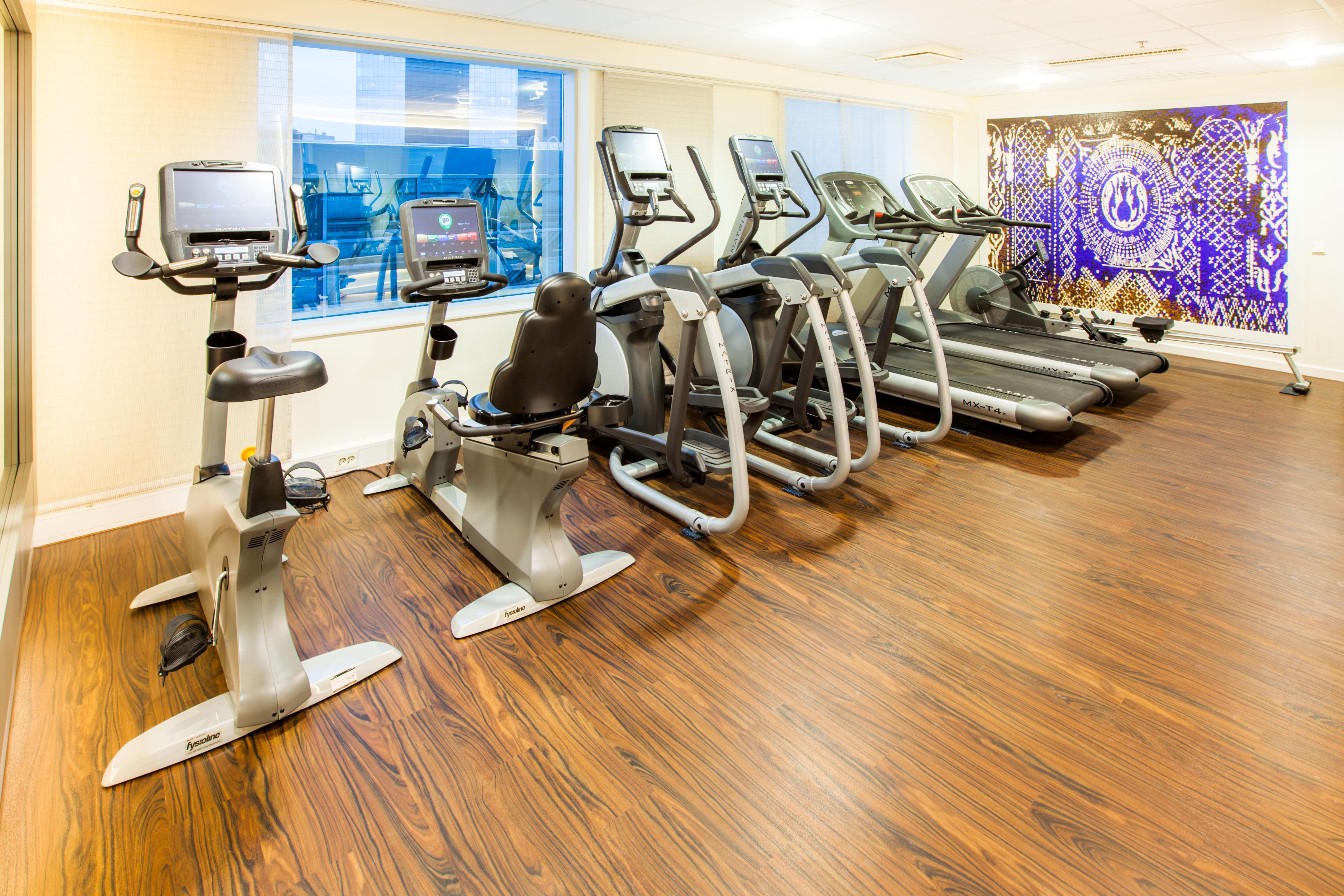 فندق راديسون بلو سكاي تالين المظهر الخارجي الصورة The photo shows a fitness room featuring various exercise equipment. There are several machines lined up, including elliptical trainers and treadmills. The floor has a warm wooden finish, and large windows allow natural light to brighten the space. A